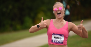 Fox Cities Marathon woman running in pink with thumbs up.