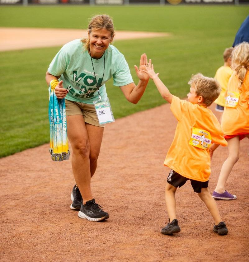 Fox Cities Marathon Kids Fun Run volunteer and kid high fiving.