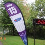 Fox Cities Marathon Course Connection March 2026 mile marker 15 flag with grass and timer.