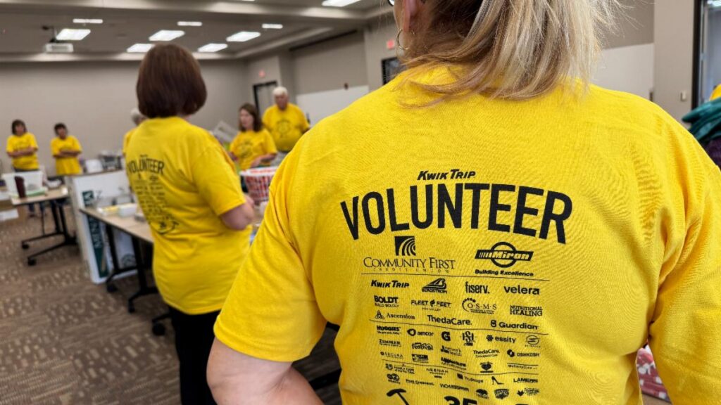 Fox Cities Marathon Volunteer Team filling goodie bags, back of two volunteers wearing yellow shirts.